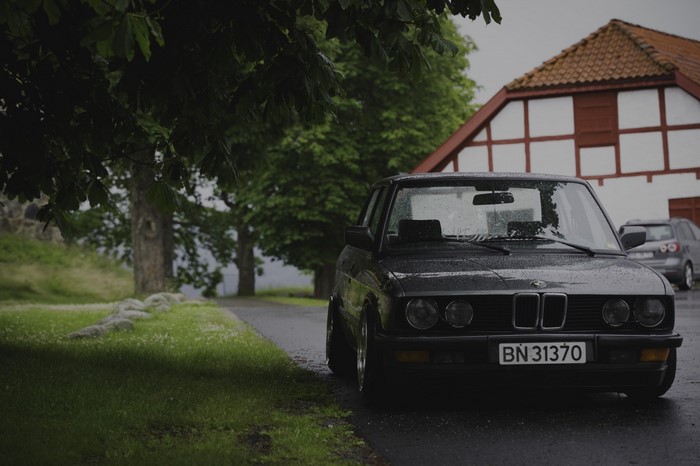 BMW E28 Sedan parked on a wet road in front of a building