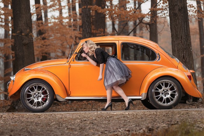 Woman applying makeup in an orange Volkswagen Beetle