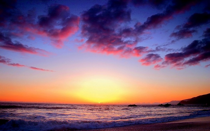 Sunset over the ocean with colorful clouds and waves