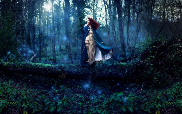 Woman with bow and arrow in a dark forest