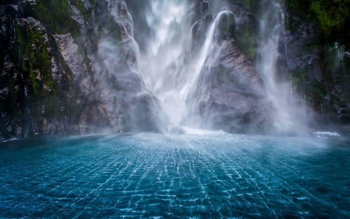 Waterfall cascading into a blue body of water in Milford Sound