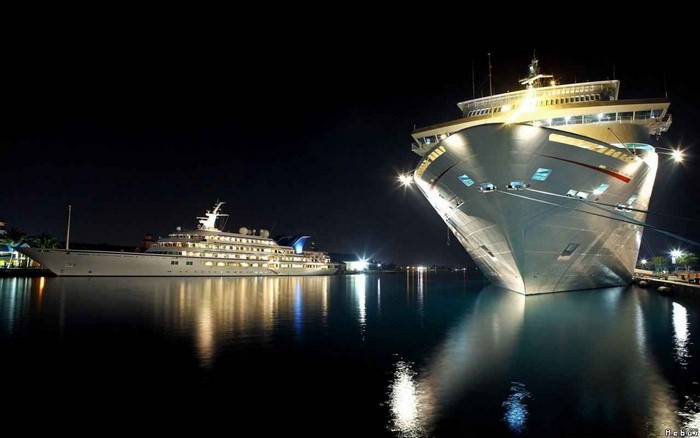 Two large ships docked at night with reflections in the water