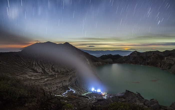 Volcanic crater lake at dawn with star trails