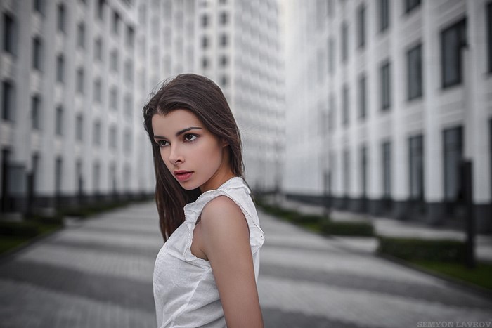 Woman in white top posing outdoors near buildings