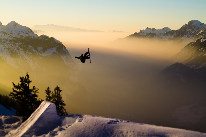 Snowboarder jumping over a foggy mountain valley at sunset