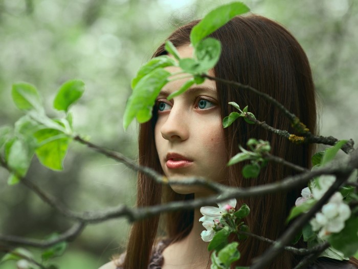 Girl with blue eyes behind leaves and flowers