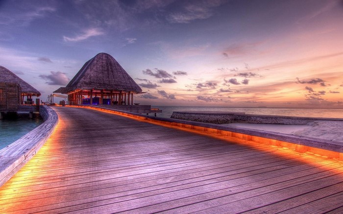 Wooden walkway to huts at sunset in the Maldives