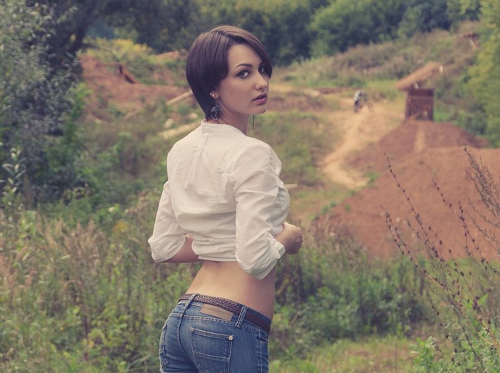 Woman in jeans and white shirt looking back outdoors