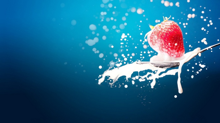 Strawberry splashing into milk on a spoon