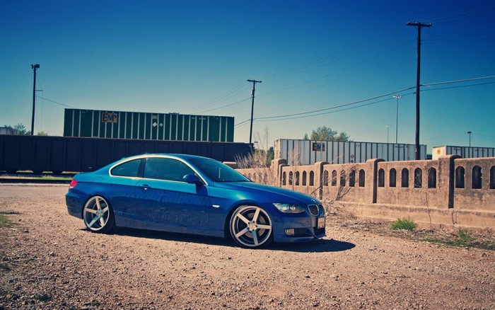Blue BMW 3 Series Coupe parked on gravel near train cars