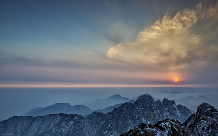 Snowy mountain range at sunset with sun rays