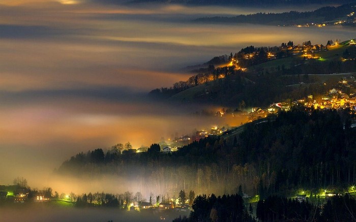 Nighttime village lights through fog on hills