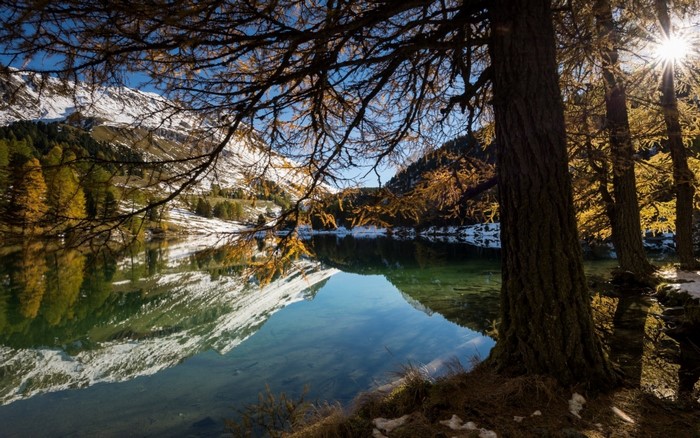 Autumnal lake reflection with snow-capped mountains and sun rays