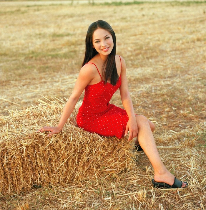 Kristin Kreuk sitting on a hay bale in a field