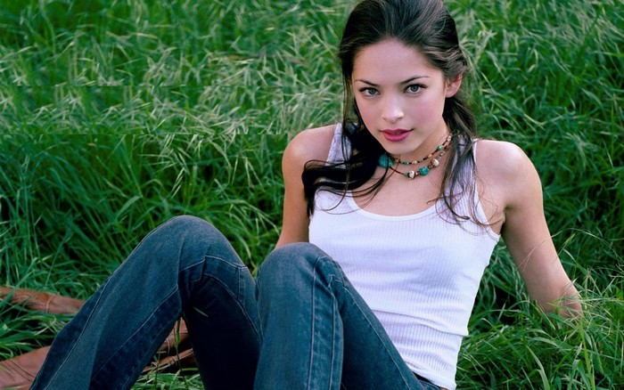 Kristin Kreuk sitting in grass wearing jeans and white top