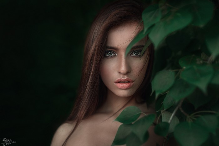 Woman with long brown hair peeking through green leaves