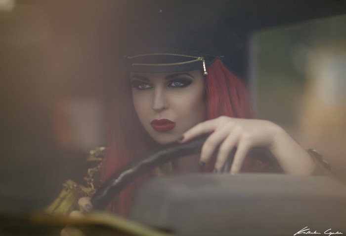 Woman with red hair wearing a hat driving a car
