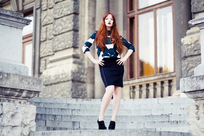 Redhead woman in patterned top and black skirt on stairs