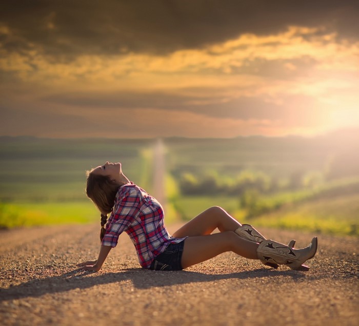 Woman in plaid shirt and cowboy boots on a road at sunset