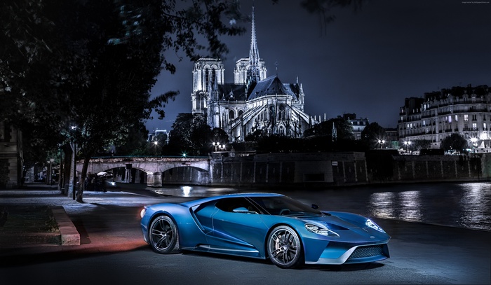 Blue Ford GT parked by the Seine River at night with Notre Dame Cathedral