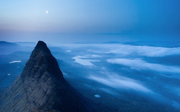 Mountain peak with moon over misty valley and lakes