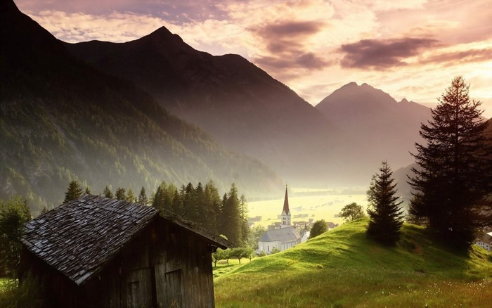 Alpine village with church and mountains at sunrise