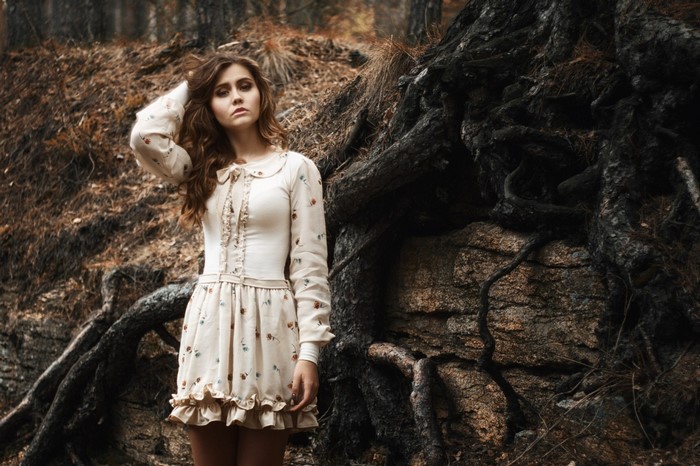 Woman in floral dress standing near tree roots in forest