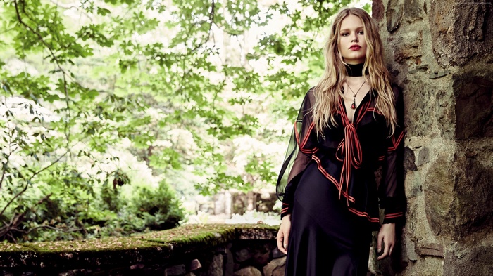 Anna Ewers leaning against a stone wall in a forest