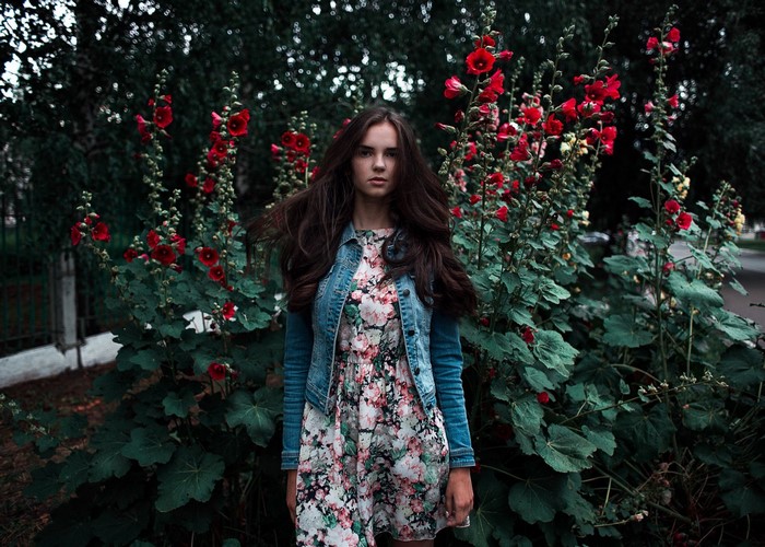 Young woman in floral dress and denim jacket among red flowers