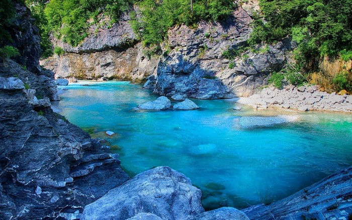 Turquoise river flowing through a rocky gorge with green trees
