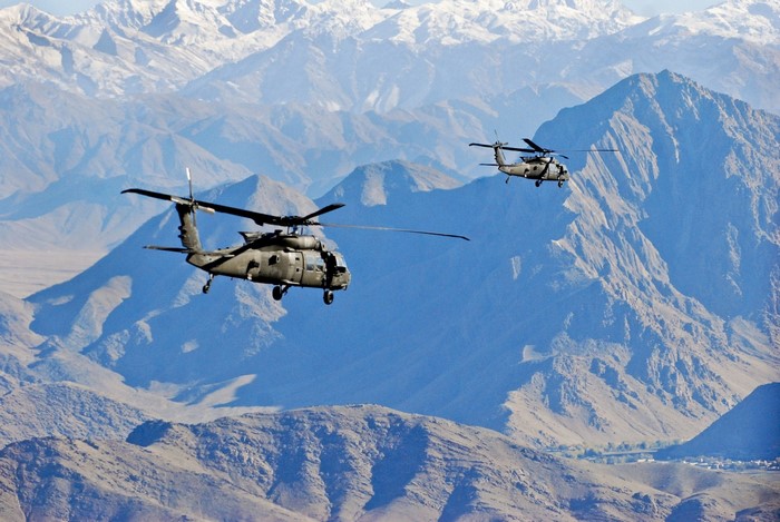 Two US Army Sikorsky UH-60 Black Hawk helicopters flying over mountains