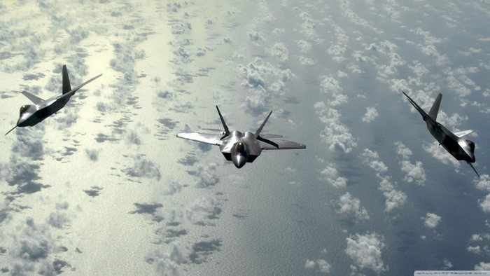 Three F-22 Raptor fighter jets flying over clouds