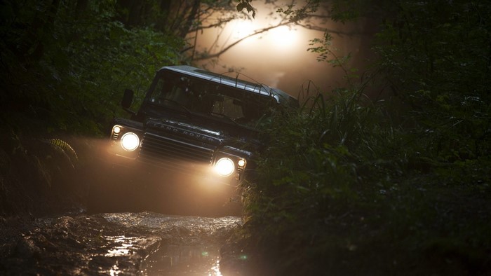 Land Rover driving through a foggy forest at night
