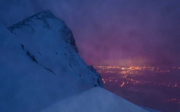Snowy mountain peak overlooking a city at dusk