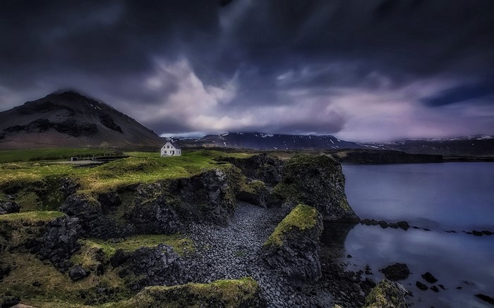 White house on a rocky coast in Iceland under stormy clouds