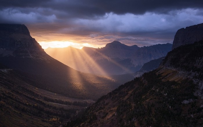 Sun rays breaking through clouds over a mountain valley at sunset