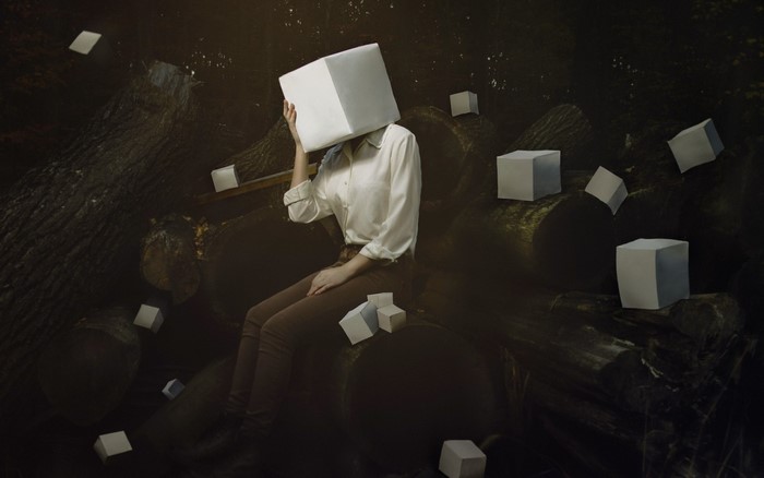 Person with cube head sitting on logs surrounded by cubes