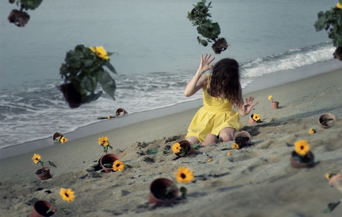 Woman in yellow dress on a beach with falling flowers