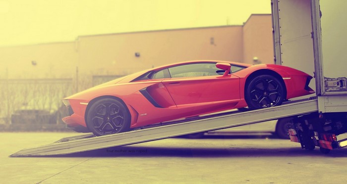Red Lamborghini Aventador being loaded onto a truck