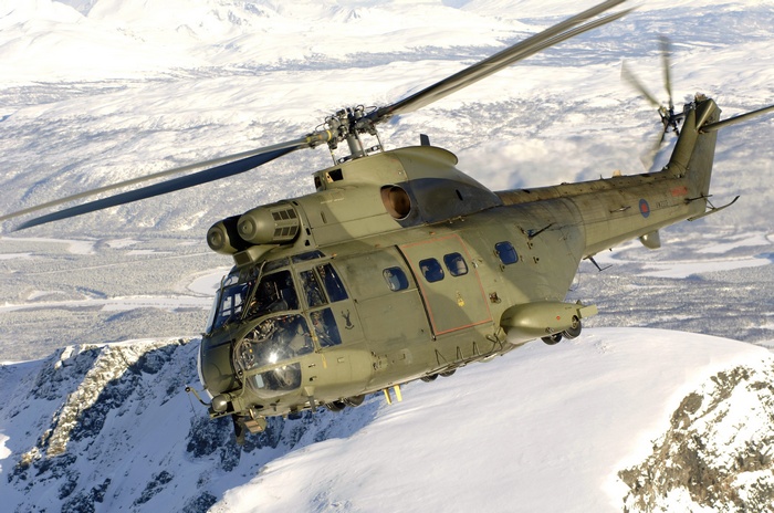Green military helicopter flying over snowy mountains