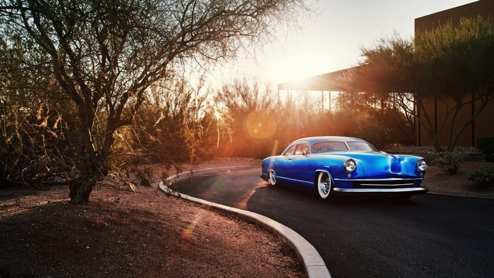 Blue classic Kaiser car driving on a road at sunrise