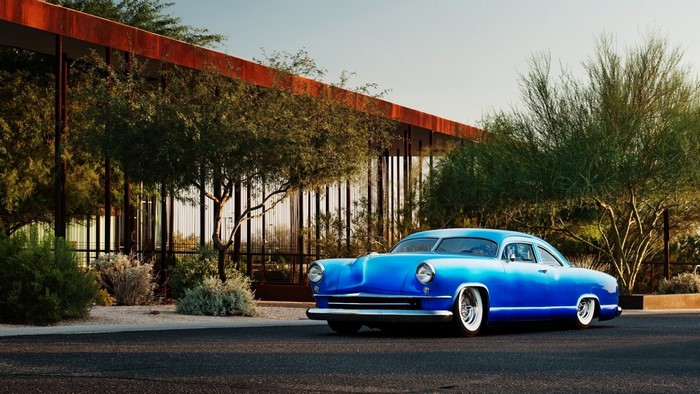 Blue classic Kaiser car parked in front of modern building