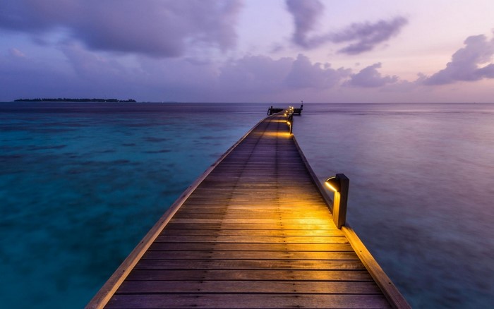 Wooden pier with lights over turquoise ocean at dusk