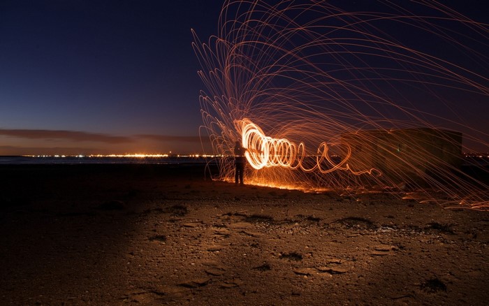 Person light painting with fire on a beach at night