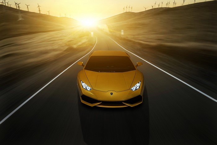 Yellow Lamborghini Huracan driving on a road with wind turbines