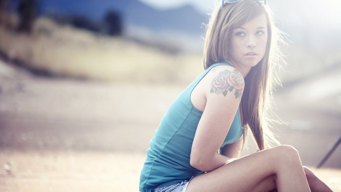 Woman with rose tattoo wearing blue tank top and sunglasses