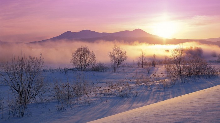 Winter sunrise over misty mountains and snow-covered landscape