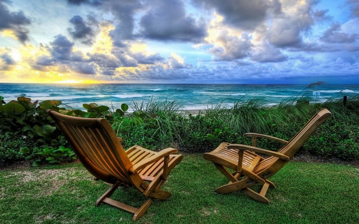 Two wooden chairs on a lawn overlooking the sea at sunset