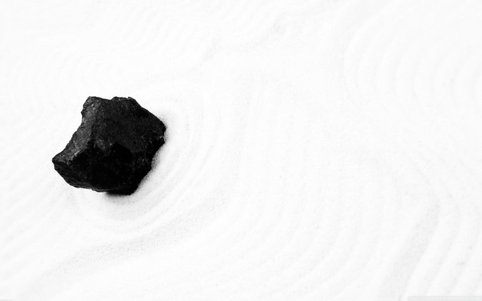 Black rock on white sand with ripples