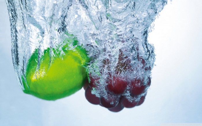 Lime and grapes splashing into water
